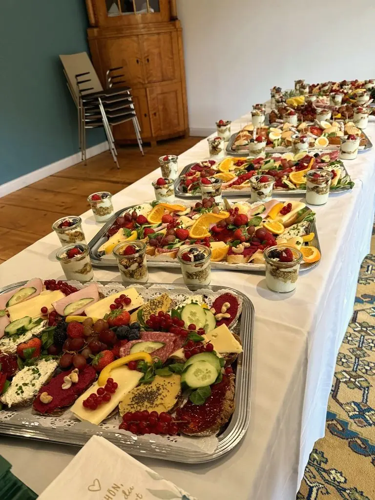 Cateringbuffet auf weißem Tisch mit belegten Platten und Dessertgläsern